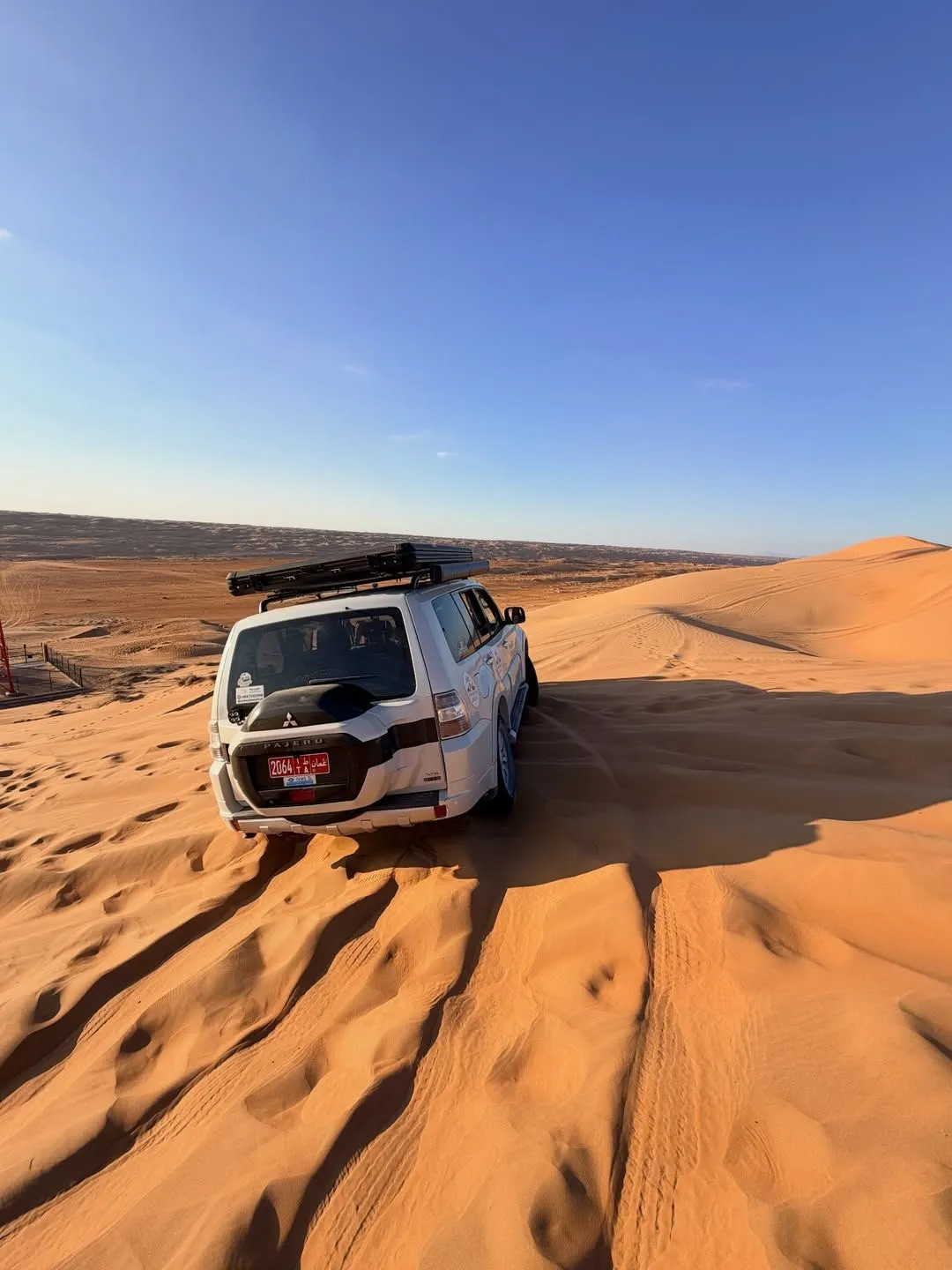 A white 4x4 vehicle driving through the sandy terrain of the Wahiba Sands.