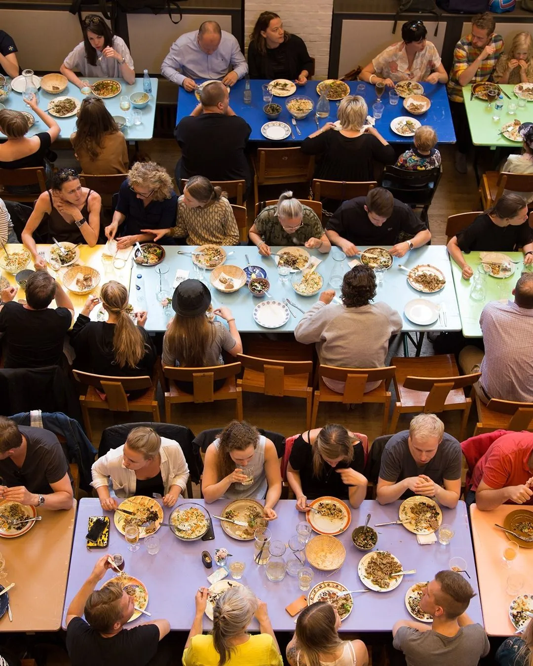 Travelers and locals eating together at long colorful tables inside the converted church Folkehuset Absalon in Copenhagen
