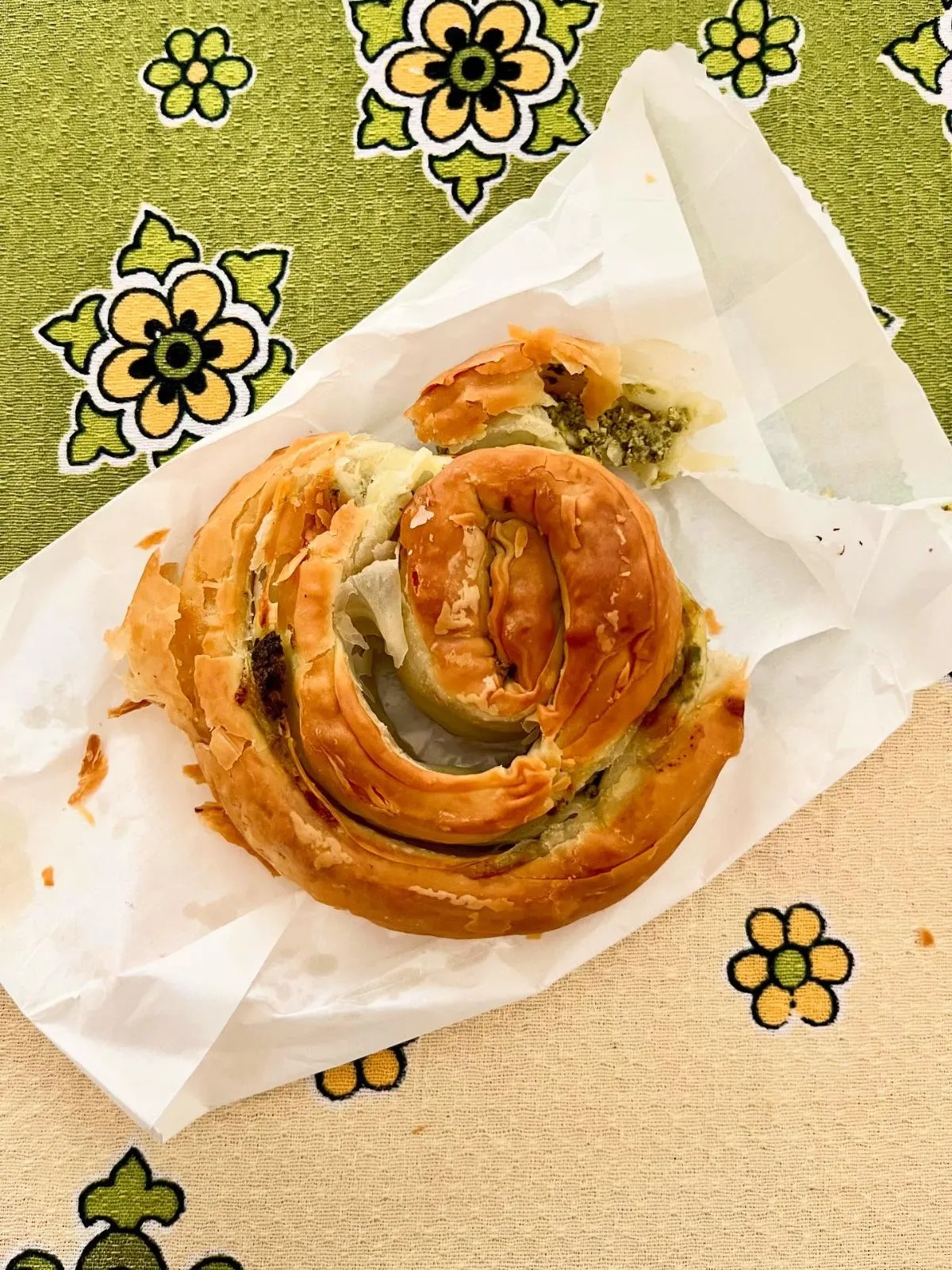 A traveler holding a fresh flaky burek pastry in front of a blue sea