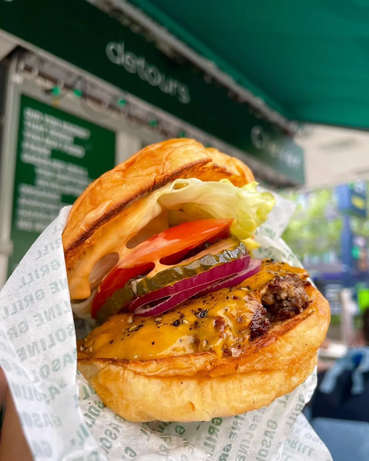 Juicy cheeseburger and fries from Gasoline Grill in Copenhagen held in front of a gas pump
