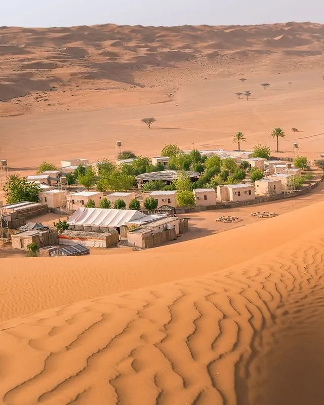 Expansive orange and gold sand dunes under a clear blue sky in the Omani desert.