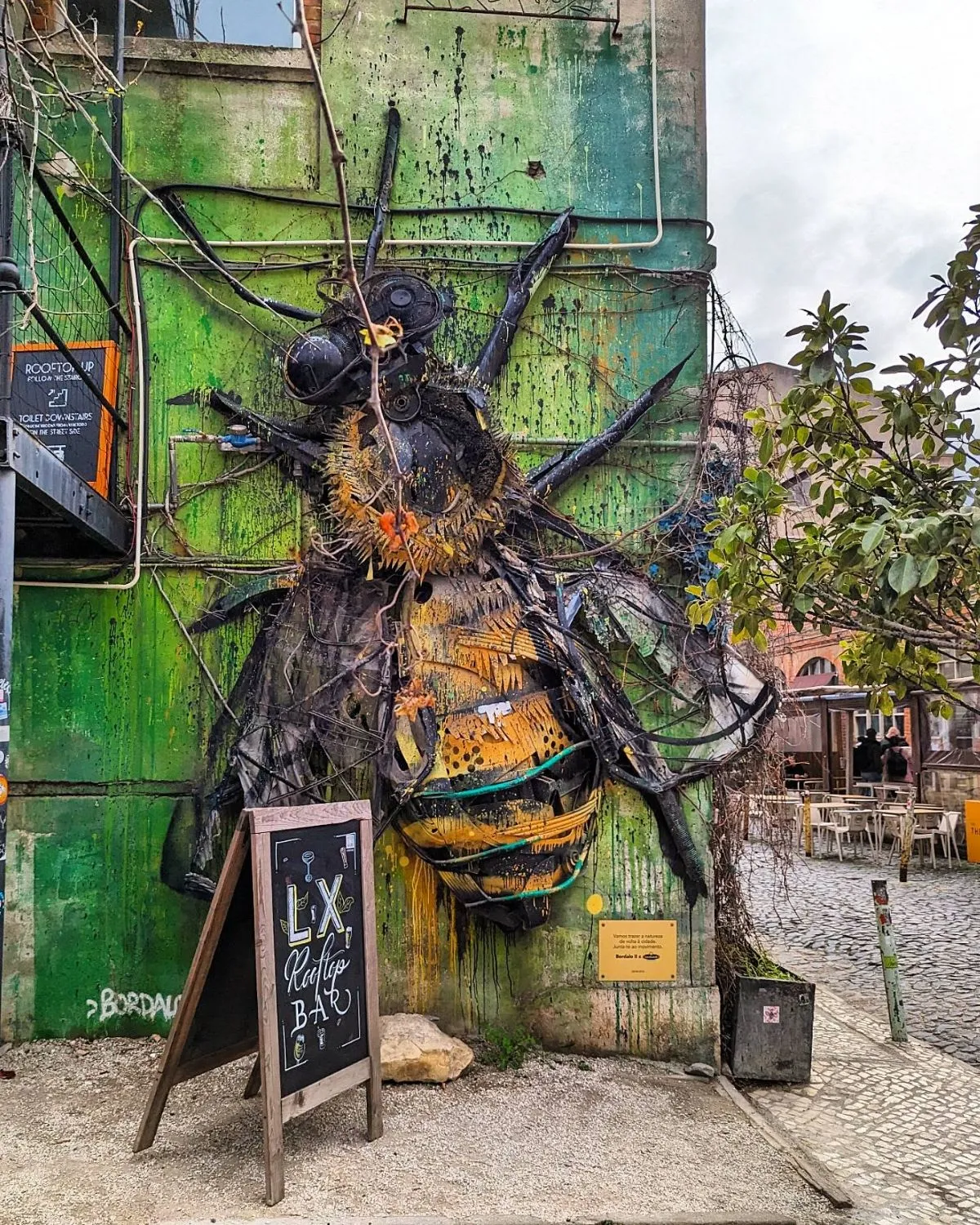 Tourists walking down the cobblestone street of LX Factory in Lisbon with the bridge overhead