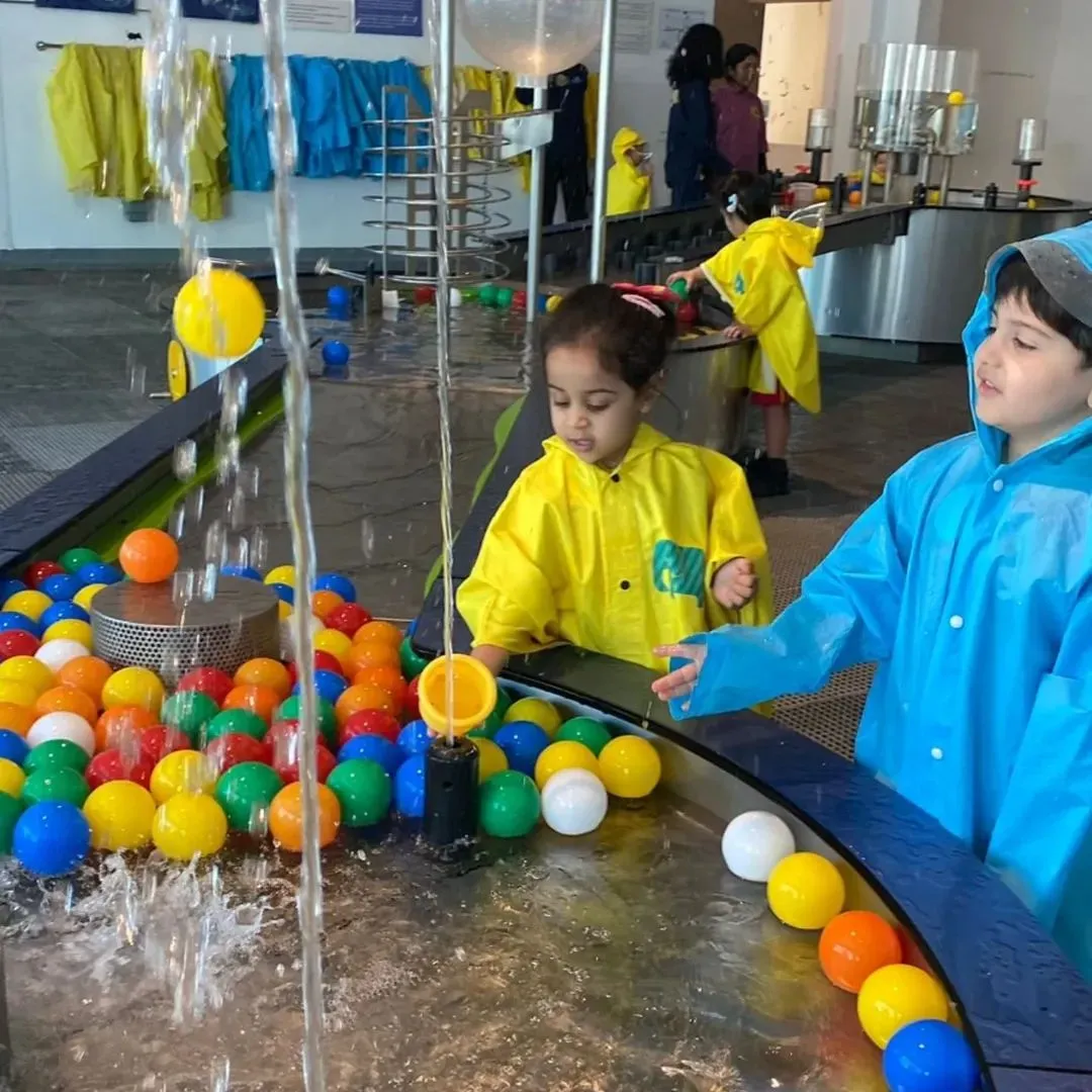 A toddler playing at a glowing blue water table inside the OliOli Experiential Museum with colorful nets in the background.