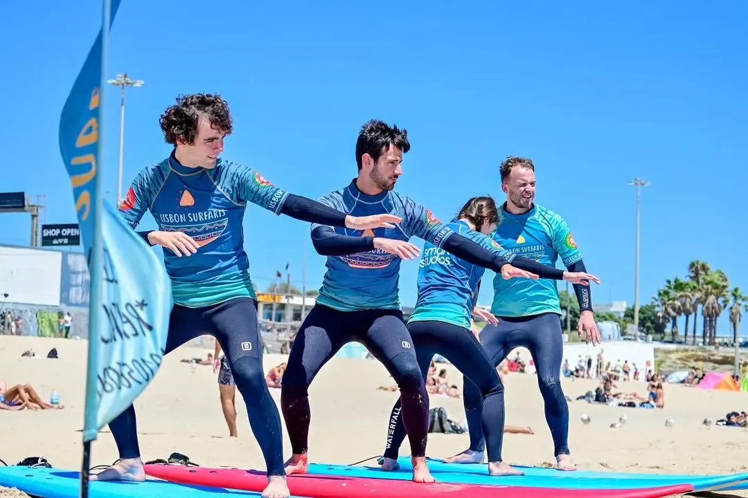 Surf instructor teaching teenagers how to stand on a board on the sand at Carcavelos