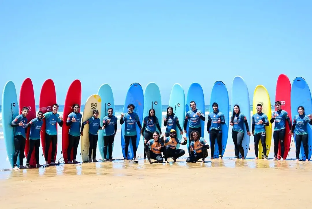 Teenagers carrying surfboards on Carcavelos beach near Lisbon with a fortress in the background