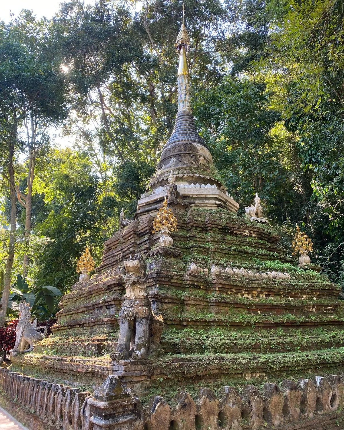 The moss-covered stone bridge and ancient structures of Wat Pha Lat in the Chiang Mai jungle.