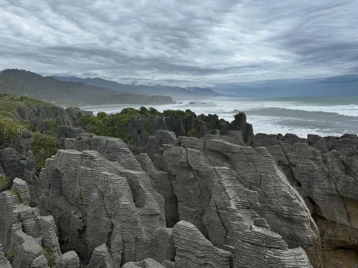 A smooth paved accessible walking path leads towards the iconic layered limestone rock formations of Punakaiki on New Zealand's West Coast.