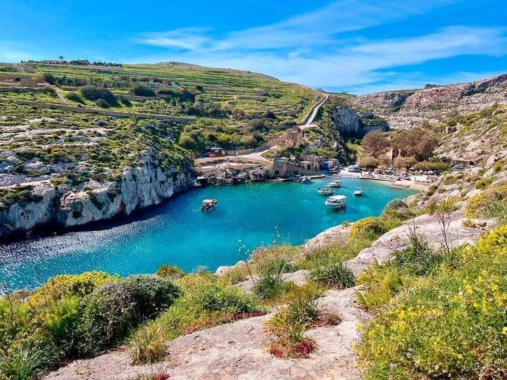 A turquoise sea inlet at Mgarr ix-Xini surrounded by high limestone cliffs.