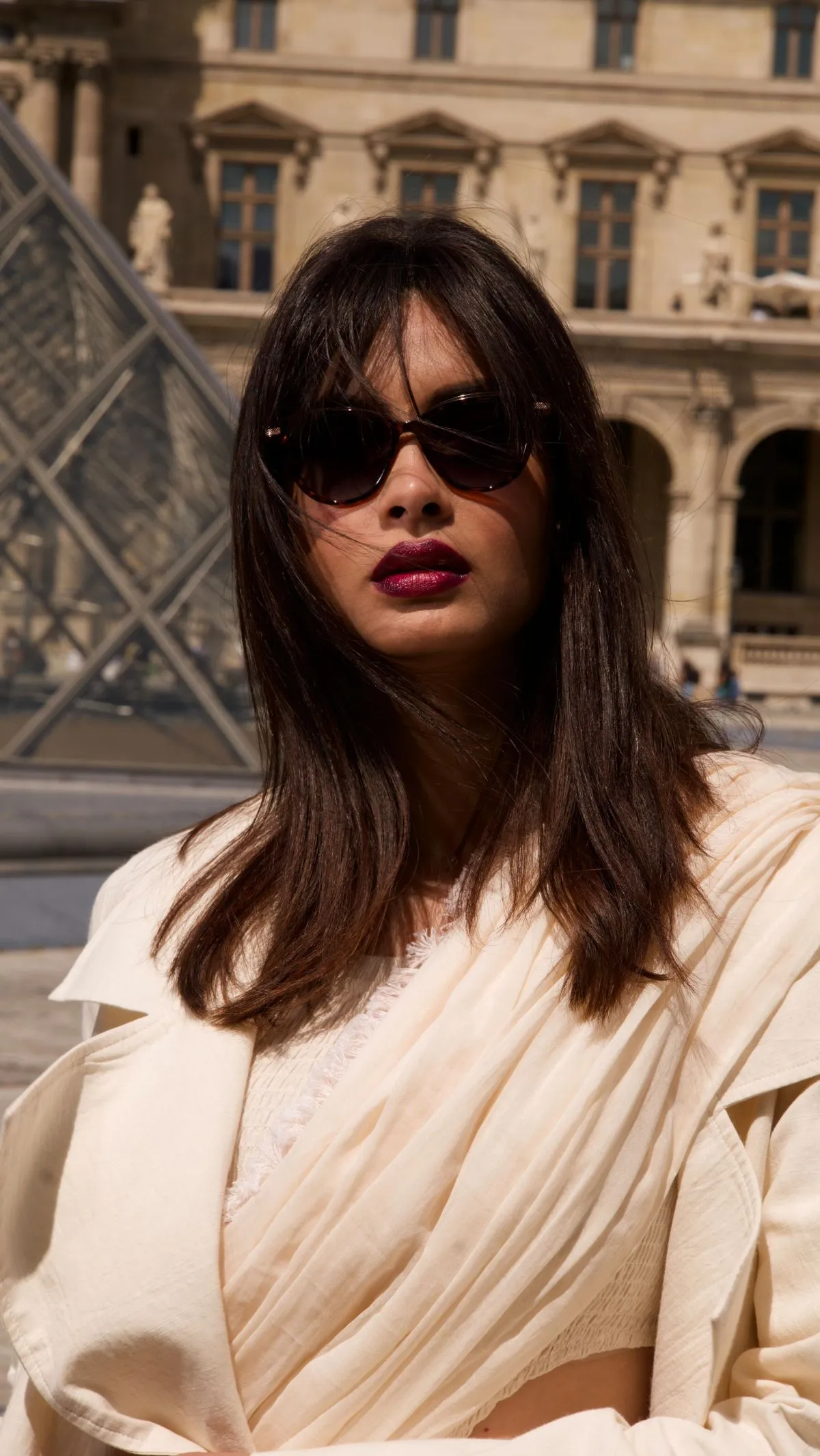 Woman wearing an effortless white linen shirt and beige tailored trousers standing by the Seine in Paris during summer.