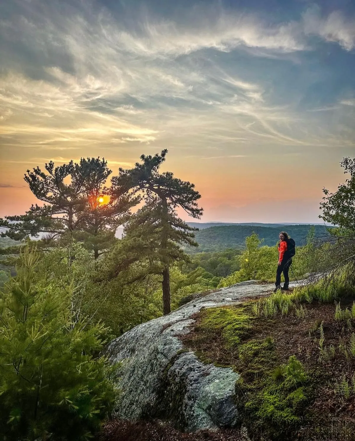 A hiker at the summit of Breakneck Ridge with a panoramic view of the Hudson River and surrounding mountains in the Hudson Highlands.