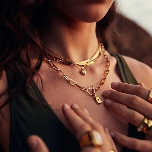 Layered gold necklaces on skin with water droplets