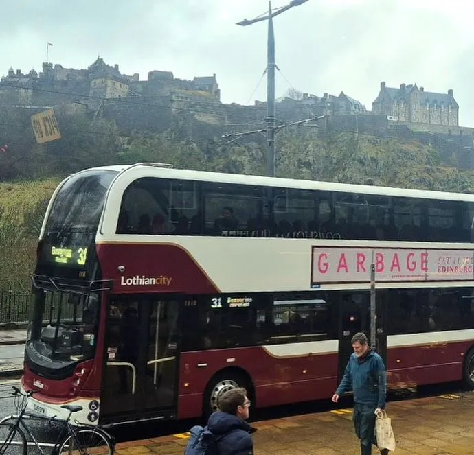 A rural Scottish village street with a green bus approaching the stop
