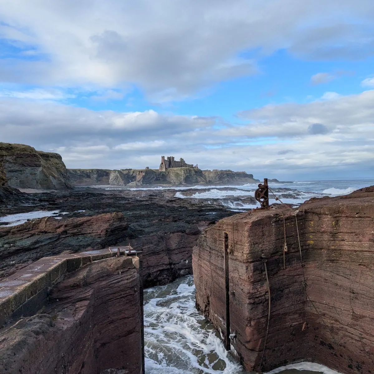 A secluded Scottish beach with golden sand, a unique sandstone harbor, and the ruins of Tantallon Castle perched on a nearby cliff.