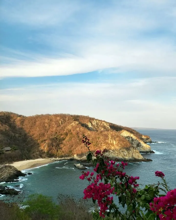 A panoramic view of a hidden golden sand beach cove with turquoise water and green cliffs on the Oaxaca coast.