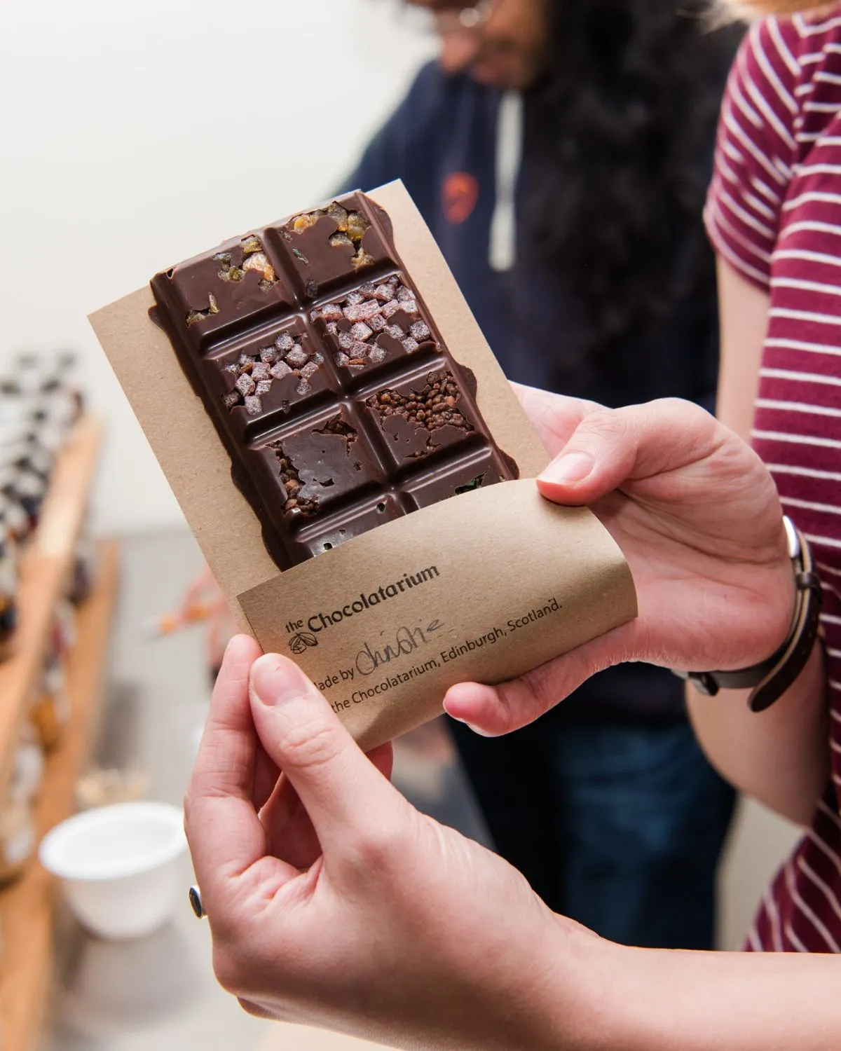 Hands adding artisanal toppings to a freshly poured chocolate bar during a workshop at the Edinburgh Chocolatarium.