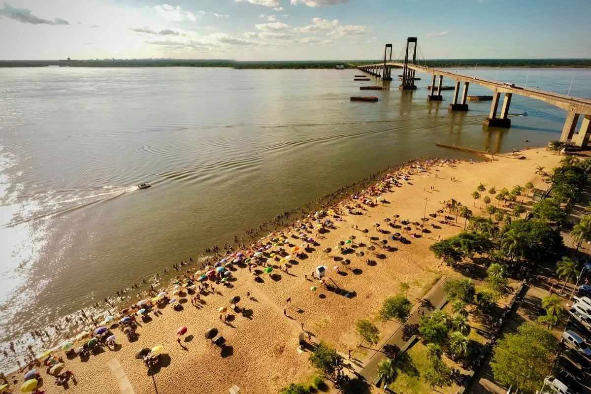A secluded river beach with golden sands and dramatic rust-colored sandstone cliffs along the Paraná River in Corrientes, Argentina.