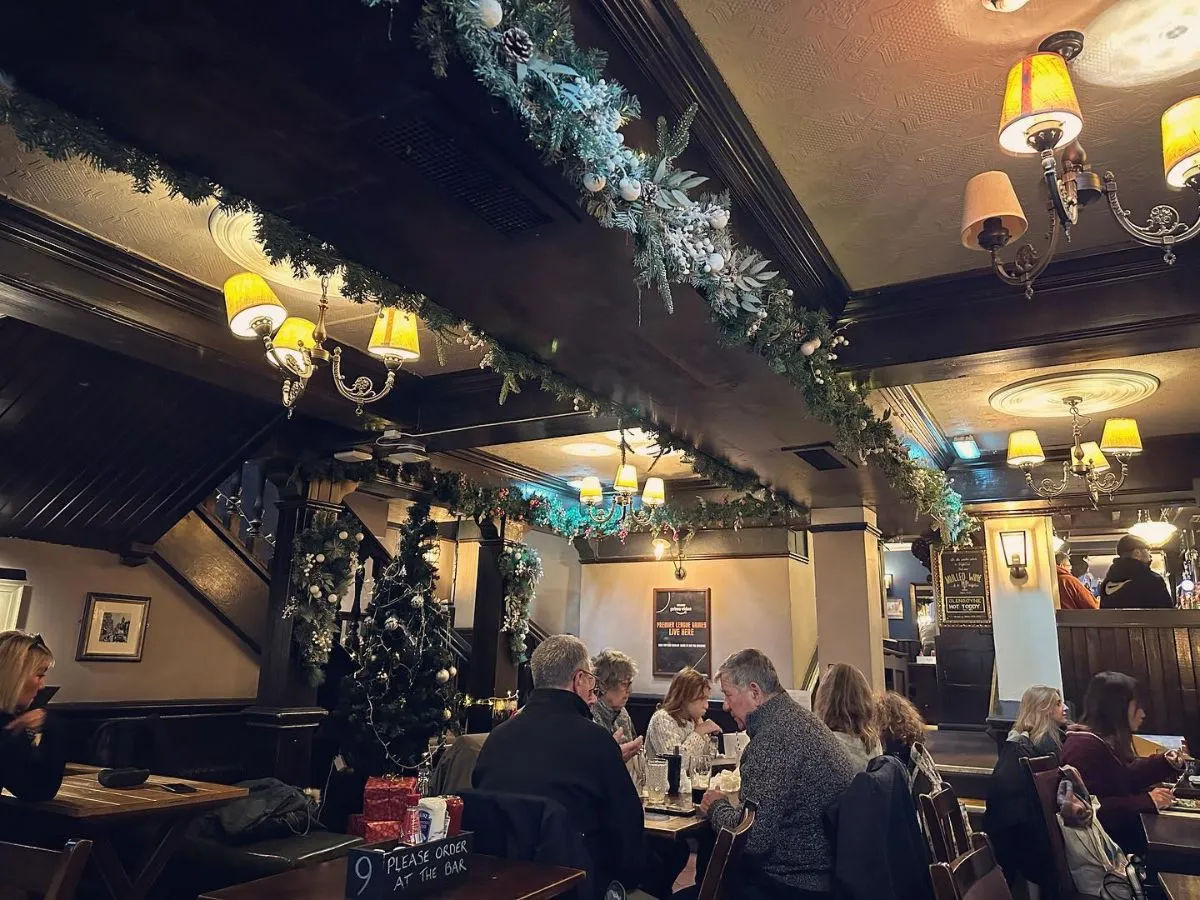A wooden table inside an Edinburgh pub featuring a pint of beer and an open poetry book