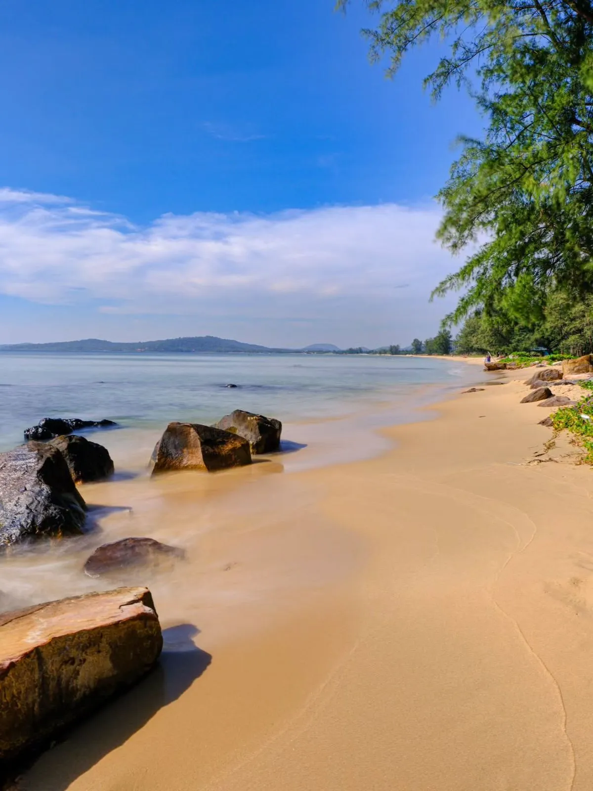 A secluded golden sand beach with calm turquoise water and lush green trees on Phu Quoc Island.