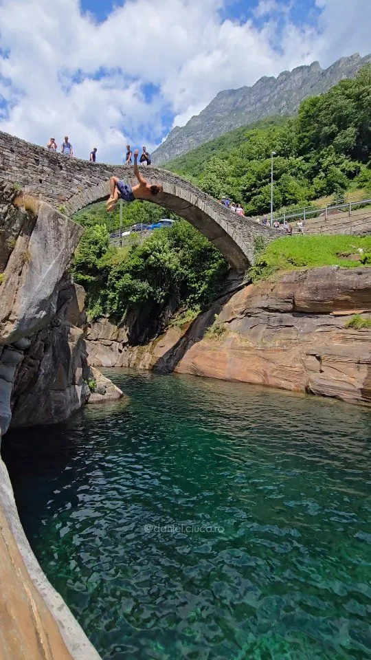The historic stone double-arched bridge Ponte dei Salti over the vibrant emerald water of the Verzasca River in Switzerland.