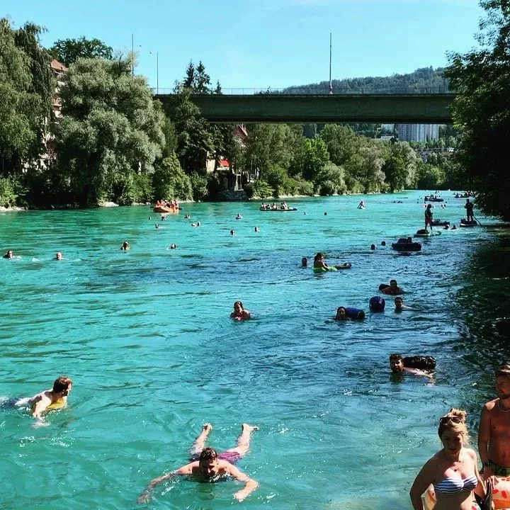 Swimmers drifting down the turquoise Aare River in Bern using colorful fish-shaped dry bags with the historic city in the background.