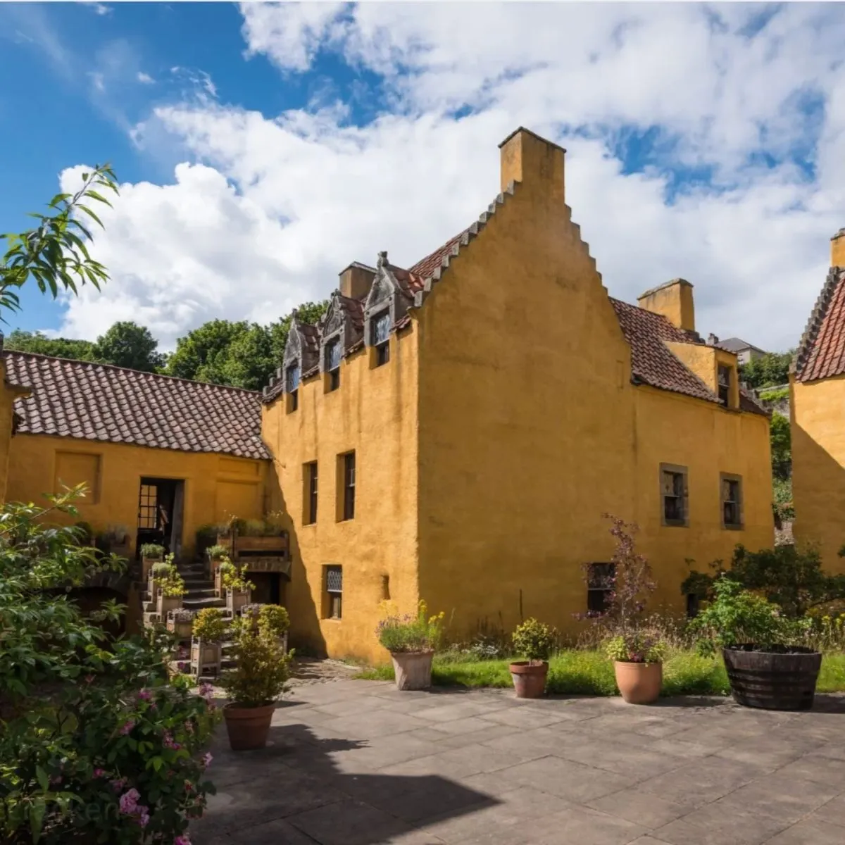 The iconic 17th-century merchant house, Culross Palace, featuring its signature bright ochre walls and cobblestone street.