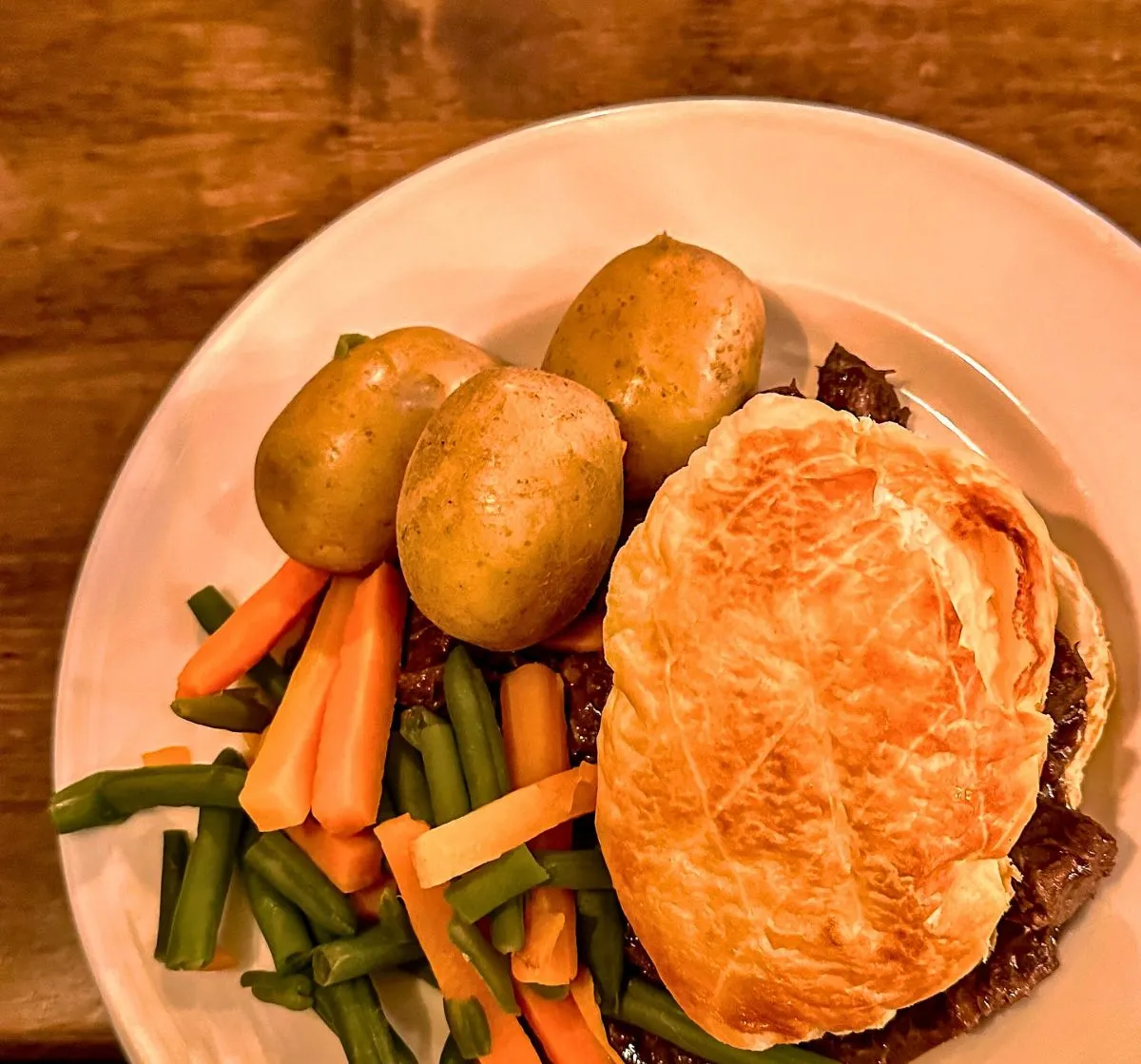 Close up of a freshly baked traditional Scottish meat pie resting on a rustic wooden table