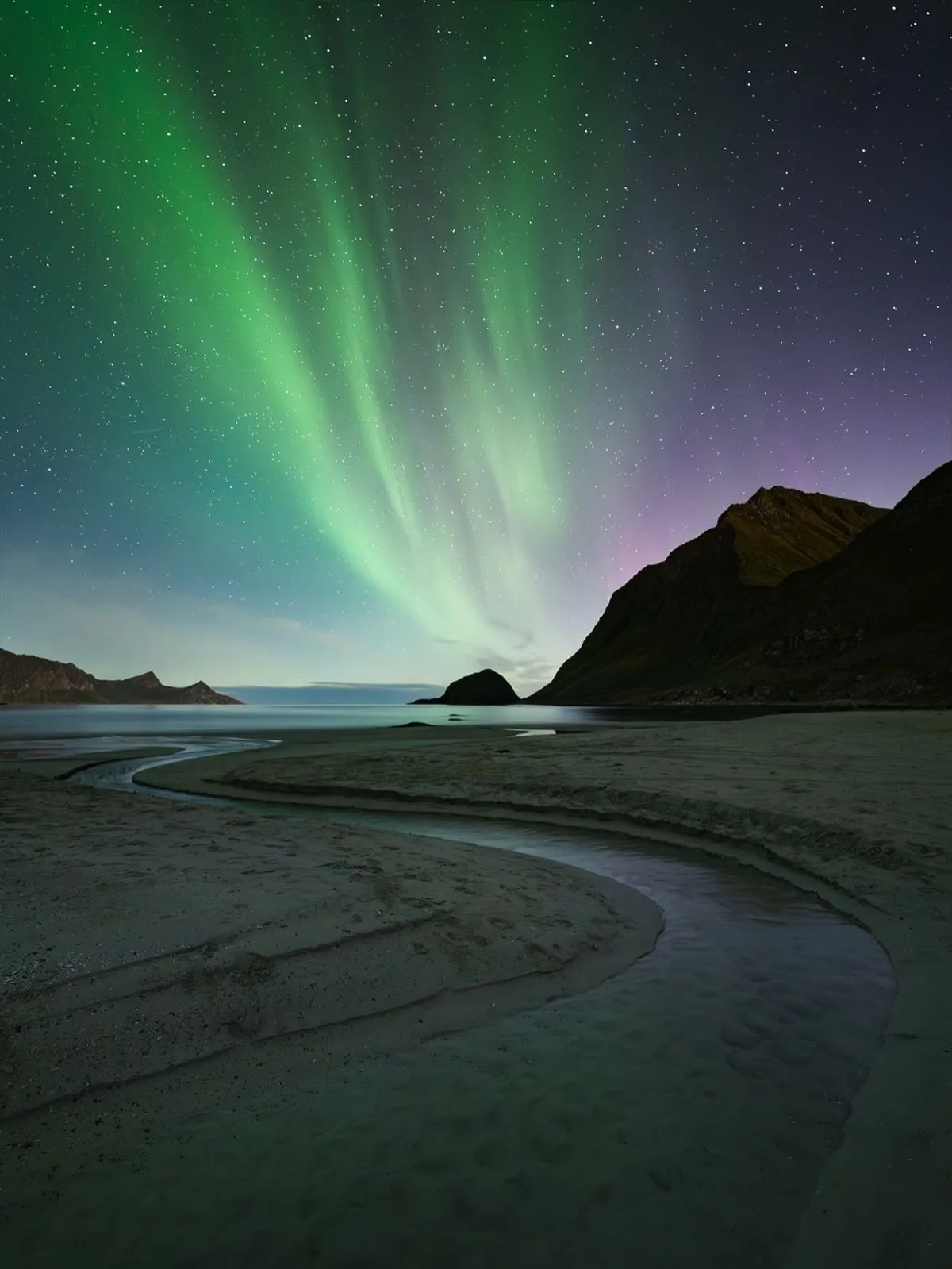 A breathtaking long exposure shot of the green Northern Lights dancing over the quiet, snowy shores of a north-facing beach in the Lofoten Islands.