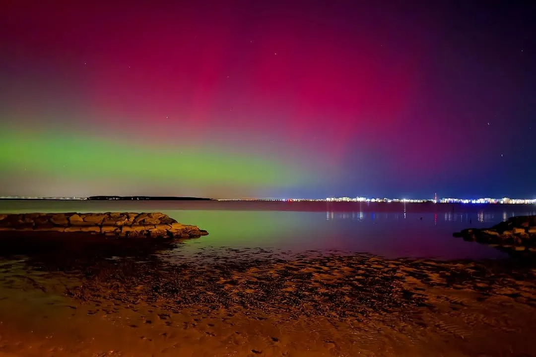 Bright green northern lights shining over the rocky shores of Myrland Beach in Lofoten
