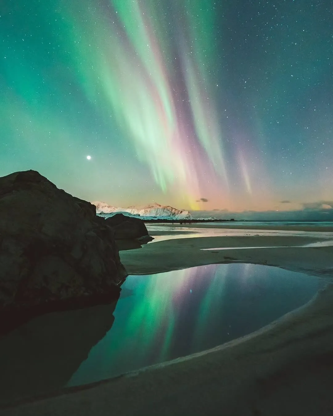 Green Northern Lights reflecting on the wet sands of Ytresand Beach in the Lofoten Islands at night