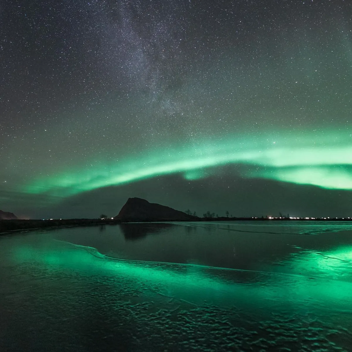 Person photographing the northern lights on a quiet snowy beach in Lofoten