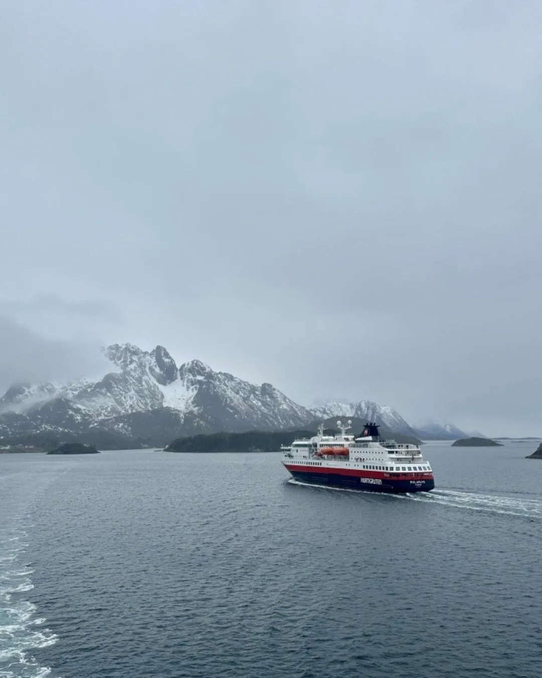 A sleek electric boat sails through the narrow, steep rocky cliffs of Trollfjord