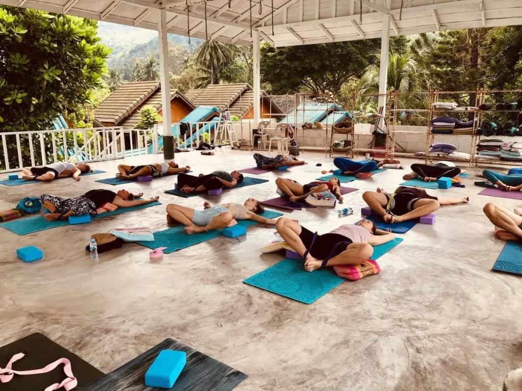 A peaceful wooden yoga shala in Sri Thanu, Koh Phangan, featuring a woman practicing yoga amidst tropical greenery and soft sunlight.