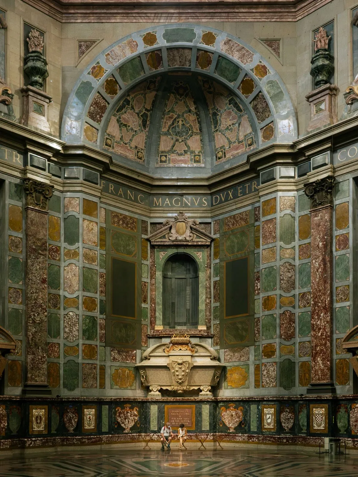 The grand dark marble interior of the Medici Chapels in Florence featuring towering Renaissance stone sculptures and shadows.
