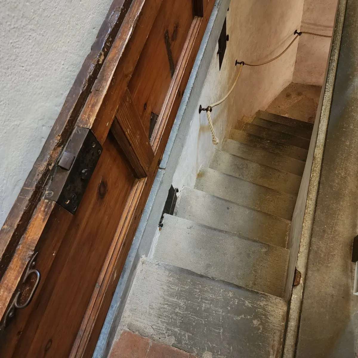 A narrow, historic stone spiral staircase descending into a dimly lit Florentine crypt with warm, soft lighting.