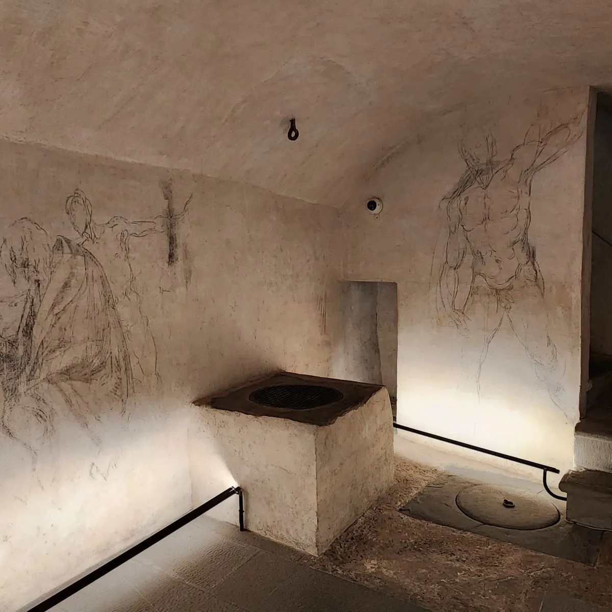 An open stone trapdoor on a marble floor inside the Medici Chapels in Florence, showing a narrow, dimly lit staircase descending into the secret room.