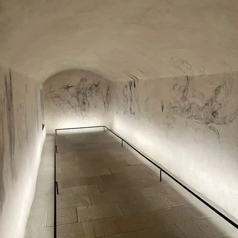 A close-up photograph of delicate Renaissance charcoal sketches on an old plaster wall inside Michelangelo