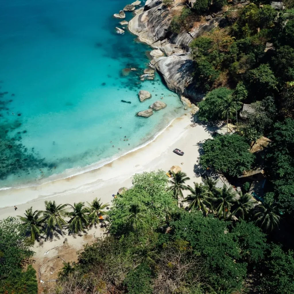 Aerial view of Sri Thanu peninsula in Koh Phangan featuring calm turquoise water, coconut palms, and peaceful eco-resorts with thatched roofs.