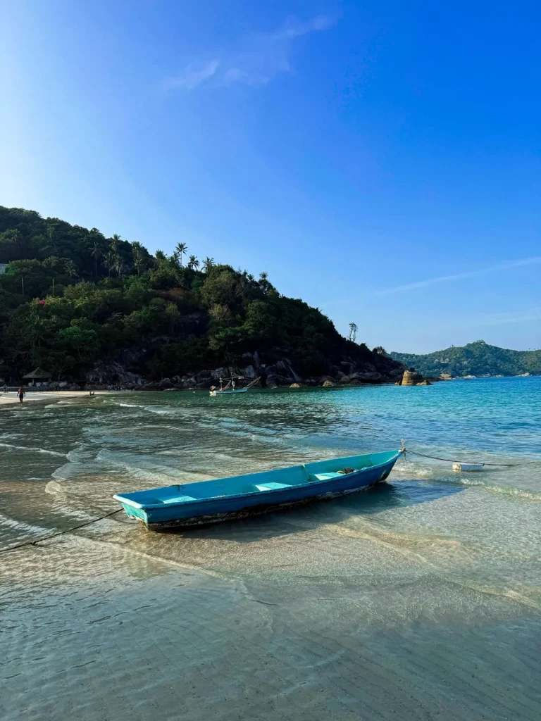 A private speedboat arriving on the pristine tropical beach of Thong Nai Pan in Koh Phangan, surrounded by crystal clear water and lush jungle mountains.